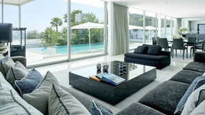 Un salon moderne doté d’une grande baie vitrée donnant sur une piscine et un espace verdoyant.