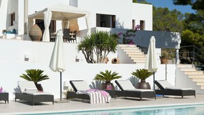 Una villa moderna con piscina, mobiliario de exterior y una escalera que lleva a una terraza.
