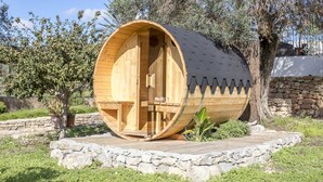 Una estructura en forma de barril de madera con una puerta y ventanas, rodeada de muros de piedra y follaje.