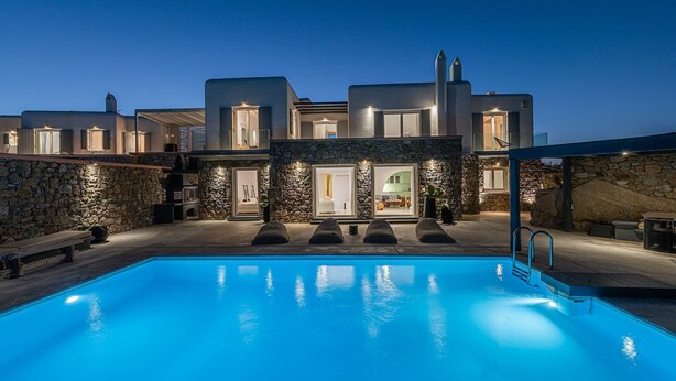 En modern villa med en swimmingpool, stenmurar och flera ingångar till huset.