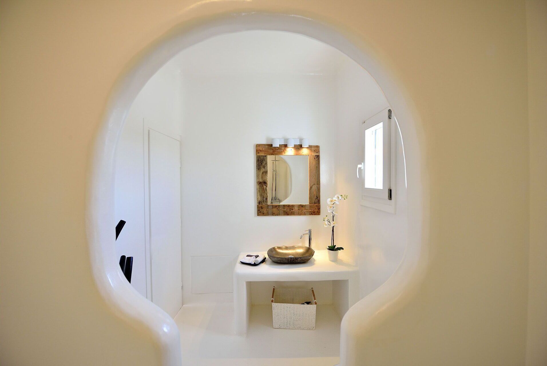 Une salle de bain avec un meuble-lavabo blanc, un miroir avec un cadre en bois, un petit lavabo et une fenêtre.