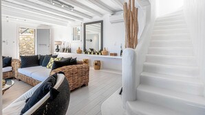 Un salon spacieux avec un canapé, des fauteuils en osier, un escalier et un mur en pierre.