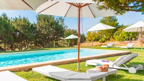 A poolside area with lounge chairs and umbrellas, surrounded by trees.