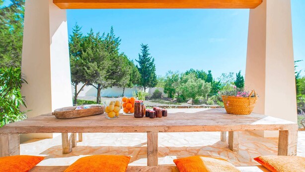 A wooden table with jars of preserves and a basket of flowers, set against a backdrop of trees and a clear sky.