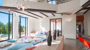 A modern interior with a sofa set, a dining area, and large windows.