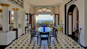 Un comedor con una mesa redonda y sillas, vista al mar y piso de baldosas.
