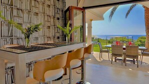 Un interior moderno con una estantería, una mesa de vidrio con sillas y vistas al océano.