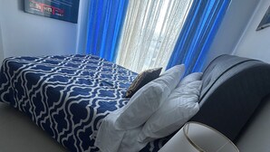 Een kamer met een bed, een bedlampje, een aan de muur bevestigde televisie en blauwe gordijnen.