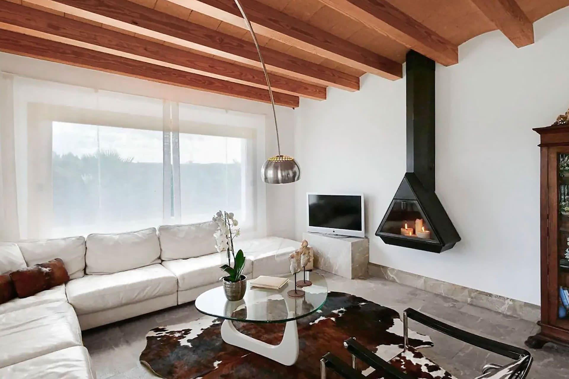 A modern living room with a white sofa, a glass coffee table, a leather rug, a TV, and a fireplace.