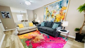 Un salon avec un tapis coloré, un canapé gris et un coin repas à l’arrière-plan.