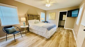Une chambre à coucher avec un lit, une chaise, une petite table et un ventilateur de plafond.