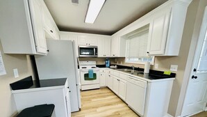 Une cuisine compacte avec des meubles blancs, un four à micro-ondes, une cuisinière et un évier.