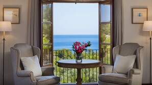 A room with two armchairs facing a large window with a view of the ocean.