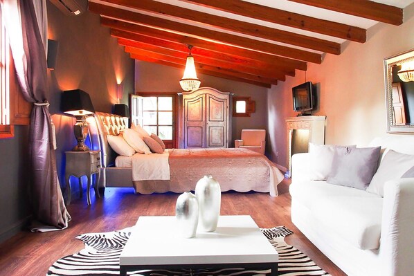A bedroom with a bed, a white sofa, a zebra-patterned rug, a wooden ceiling, and a chandelier.