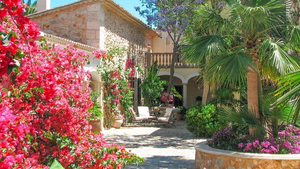 Une cour avec un bâtiment en pierre, des plantes en pot et des sièges d’extérieur.
