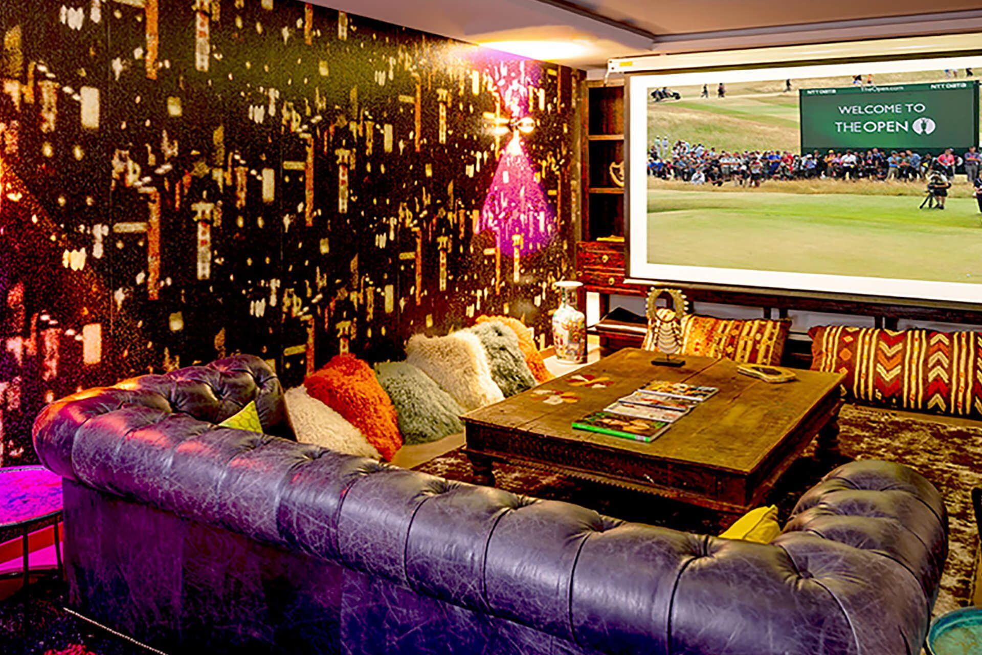 Cómoda zona de estar con un sofá de cuero, una mesa de centro con revistas y una pantalla grande mostrando un evento de golf.