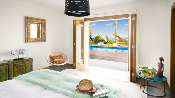 Un dormitorio con cama, una silla, una mesita con planta y vistas a una piscina y zona exterior.