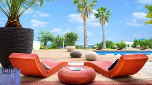 Zona junto a la piscina con dos sillas reclinables naranja, un otoman redondo y una jardinera de piedra.