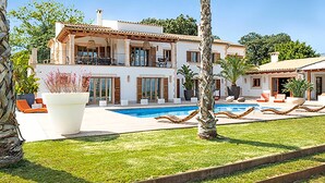 Una casa de dos pisos con piscina, mobiliario exterior y palmeras.