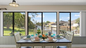 A dining area with a table set for four, large windows with a view of a residential neighborhood and a body of water. - GameRoom | Canal | Large Dock | Pool | Pets OK! 6 beds (Palm Coast)