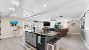 A spacious kitchen with a central island, a dining area with a high ceiling fan, and a cozy seating area with a couch and a TV. - GameRoom | Canal | Large Dock | Pool | Pets OK! 6 beds (Palm Coast)