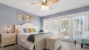 A bedroom with a bed, nightstands, a bench, and a chair. There are windows with blinds, a ceiling fan, and artwork on the wall. - GameRoom | Canal | Large Dock | Pool | Pets OK! 6 beds (Palm Coast)