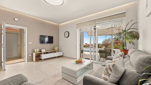 A modern living room with a sofa, coffee table, TV, and a sliding glass door leading to a balcony. - Modern Villa Novtek with Pool and Sea View (Diminići)