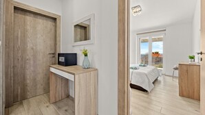 A modern bedroom with a wooden desk, a bed with a white duvet, and a large window. - Modern Villa Novtek with Pool and Sea View (Diminići)