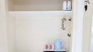 Une petite cuisine équipée d’un four à micro-ondes, d’une bouilloire et d’un grille-pain, le tout posé sur le plan de travail.