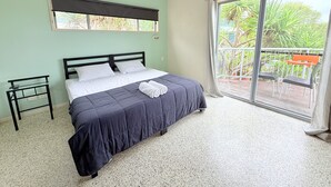 Une chambre à coucher avec un lit, une petite table de chevet, une fenêtre et un balcon avec des chaises.