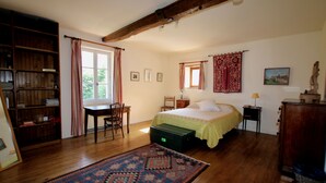 Un dormitorio con cama, escritorio, silla, estantería y ventana con cortinas.