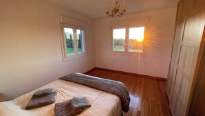 A bedroom with a bed, two windows, a chandelier, and a view of the sunset. - AS NEVEIRAS, TYPICAL GALICIAN RURAL HOUSE (Fixó)