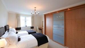 A hotel room with two beds, a desk, a chair, a chandelier, and a sliding door closet. - Turnberry Apartments 2G (Turnberry)