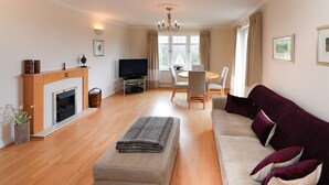 A spacious living room with a fireplace, a television, a dining area, and a sofa. - Turnberry Apartments 2G (Turnberry)