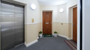 A hallway with a double door, a wooden door, and a small green plant. - Turnberry Apartments 2G (Turnberry)