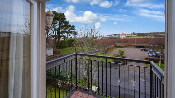 A balcony with a view of a parking area, a building in the distance, and a clear sky. - Turnberry Apartments 2G (Turnberry)