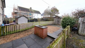 Ein Wohnhausgarten mit Ziegelpflanzkübel, Holzzaun und Gartenhaus.