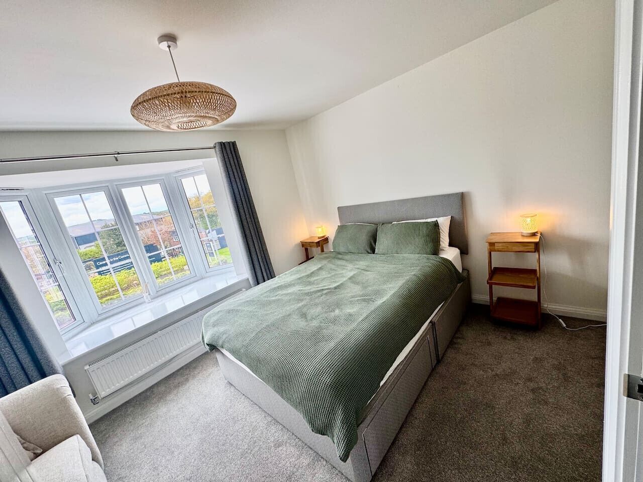 Une chambre à coucher comprenant un lit, une table de chevet, une lampe, une fenêtre avec des rideaux et un luminaire au plafond.