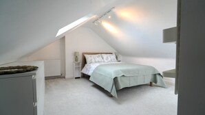 Ett sovrum med ett sluttande tak, en säng med ett vadderat överkast, ett sängbord med en lampa och ett element.