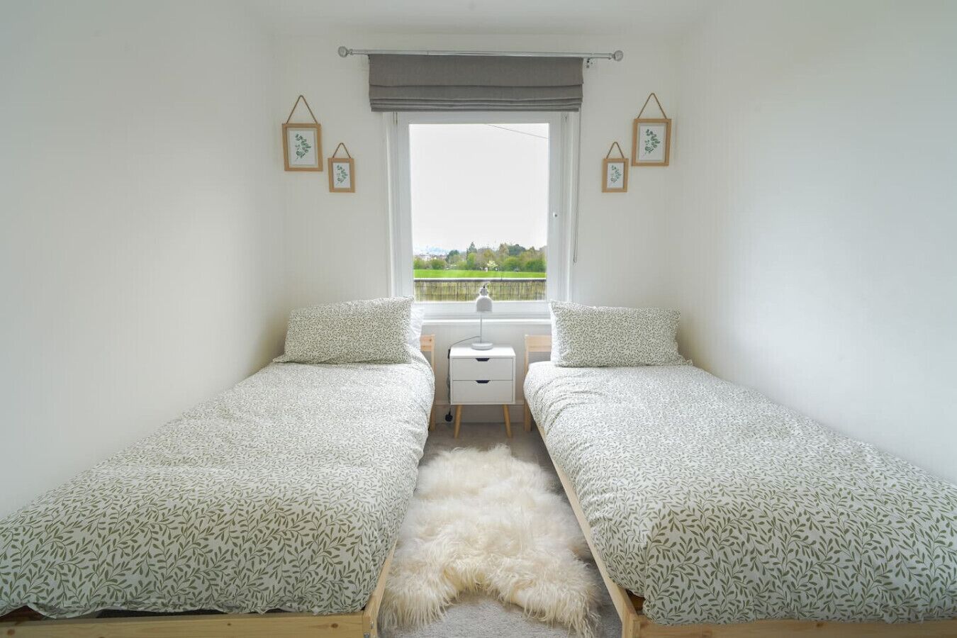 Une chambre avec deux lits simples, une petite table de chevet blanche, un tapis moelleux et une fenêtre donnant sur un paysage verdoyant.