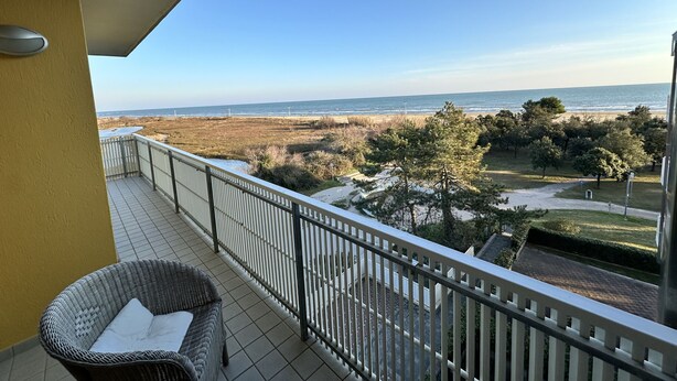 Ein Balkon mit einem Korbstuhl, Blick auf den Strand und einem klaren Himmel.