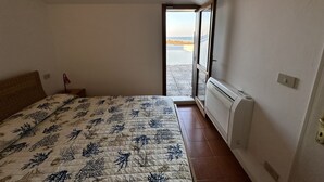 Ein Schlafzimmer mit Bett, Heizkörper, Fenster und Blick auf den Strand.