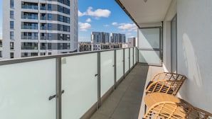 Un balcon doté d’une balustrade en verre, de chaises en osier et offrant une vue sur les immeubles de grande hauteur.