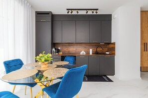 Une cuisine moderne avec des meubles de couleur sombre, un plan de travail en bois et une table à manger en verre, assortie de chaises bleues.