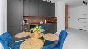 Une cuisine moderne avec des meubles de couleur sombre, un plan de travail en bois et une table à manger en verre, assortie de chaises bleues.