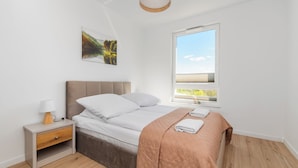 Une chambre à coucher avec un lit, une table de chevet avec une lampe, une fenêtre donnant sur un beau paysage et un tableau accroché au mur.