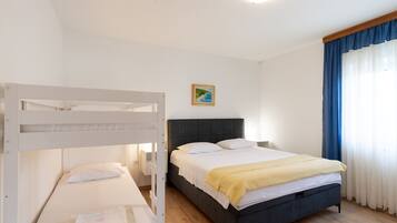 Une chambre d’hôtel avec un lit superposé, un lit simple, une table de chevet, une lampe et un tableau au mur.