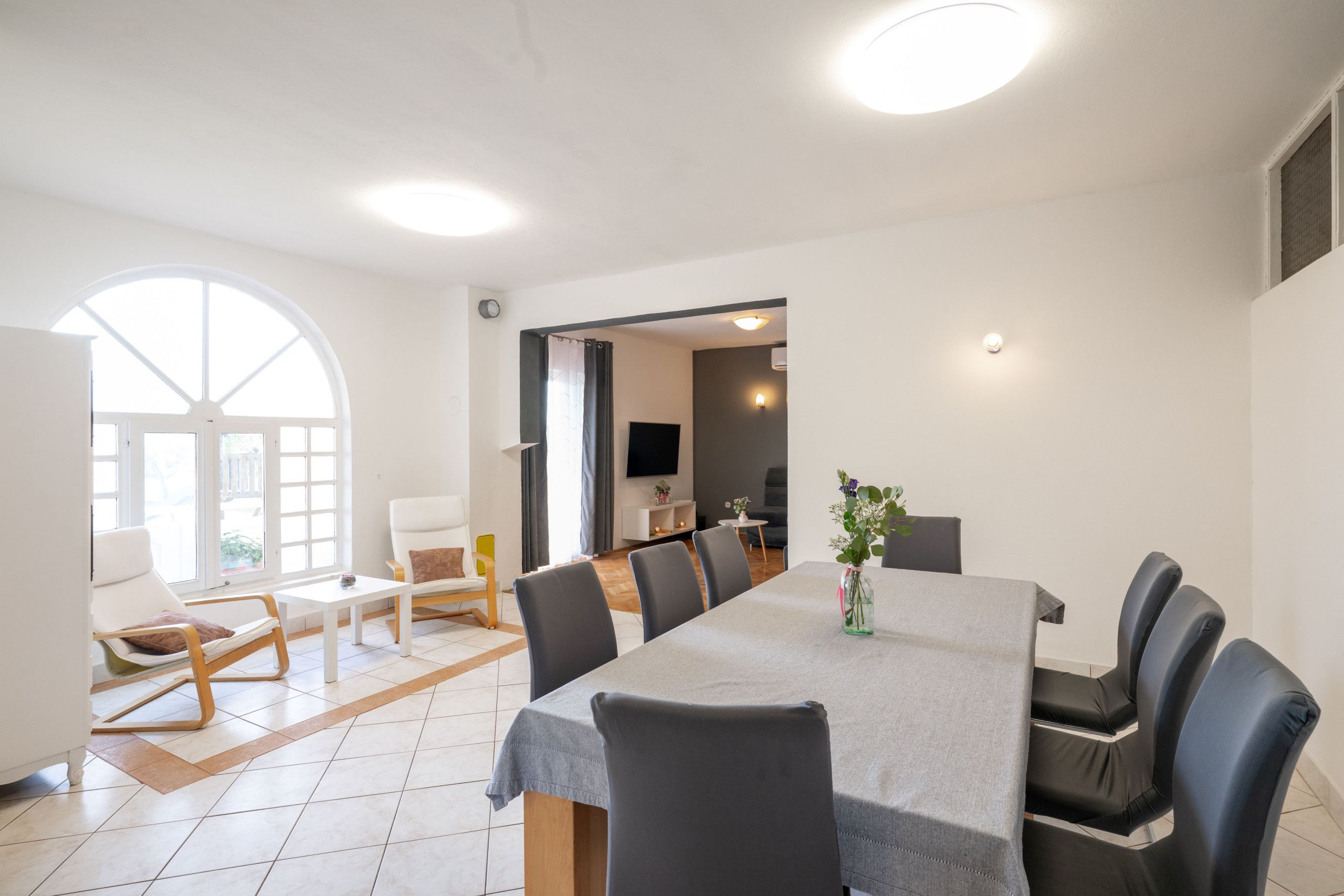 A modern dining area with a large table, chairs, and a view through an arched window.