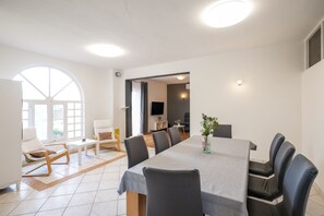 A modern dining area with a large table, chairs, and a view through an arched window. - House Rose – country house with pool (Ražanac)