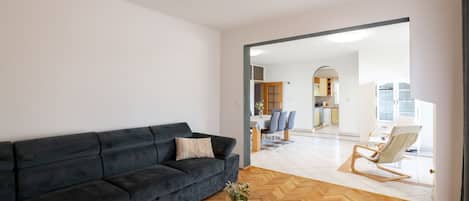 A modern living room with a dark sofa, a white coffee table, and a view into the dining area.